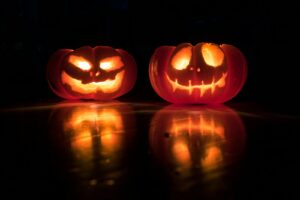 Zwei geschnitzte, beleuchtete Halloweenkürbisse vor dunklem Hintergrund